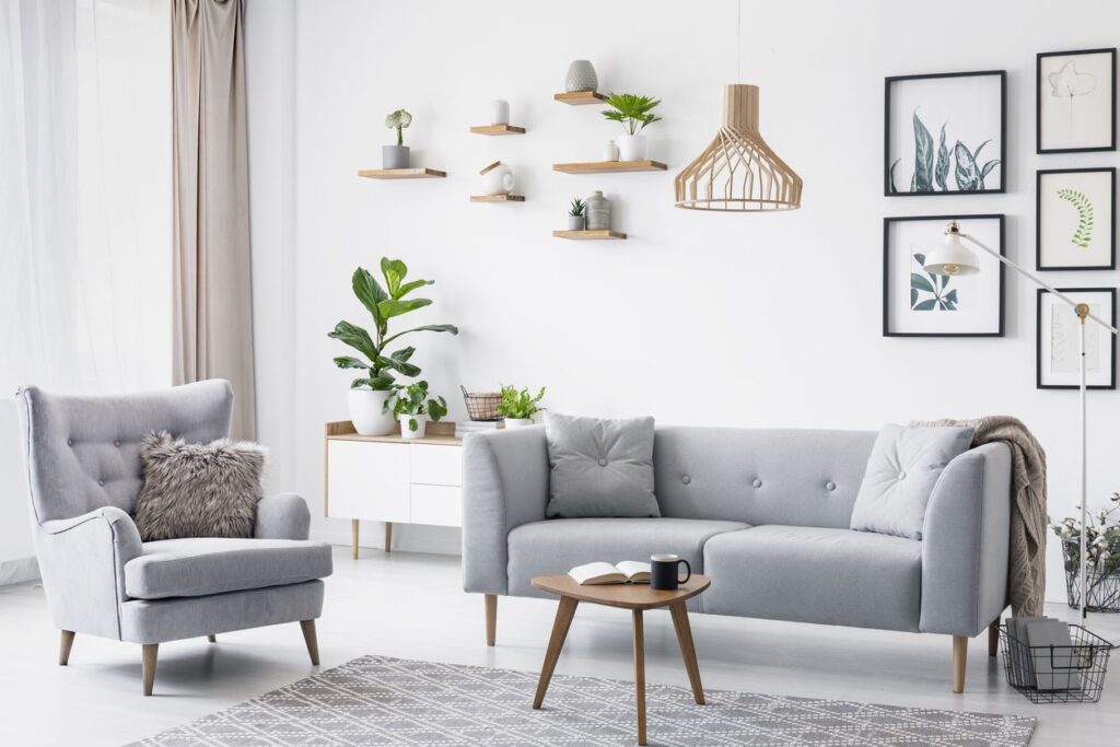 GREY ARMCHAIR NEXT TO SETTEE IN BRIGHT LIVING ROOM INTERIOR WITH POSTERS AND WOODEN TABLE. REAL PHOTO